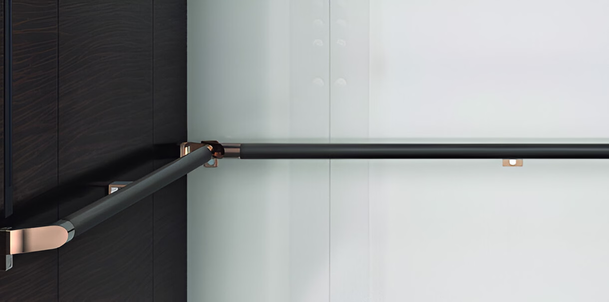 Чорний горизонтальний поручень з металевими кріпленнями кольору рожевого золота, прикріплений до темно-коричневої панелі зліва та білої стіни справа.