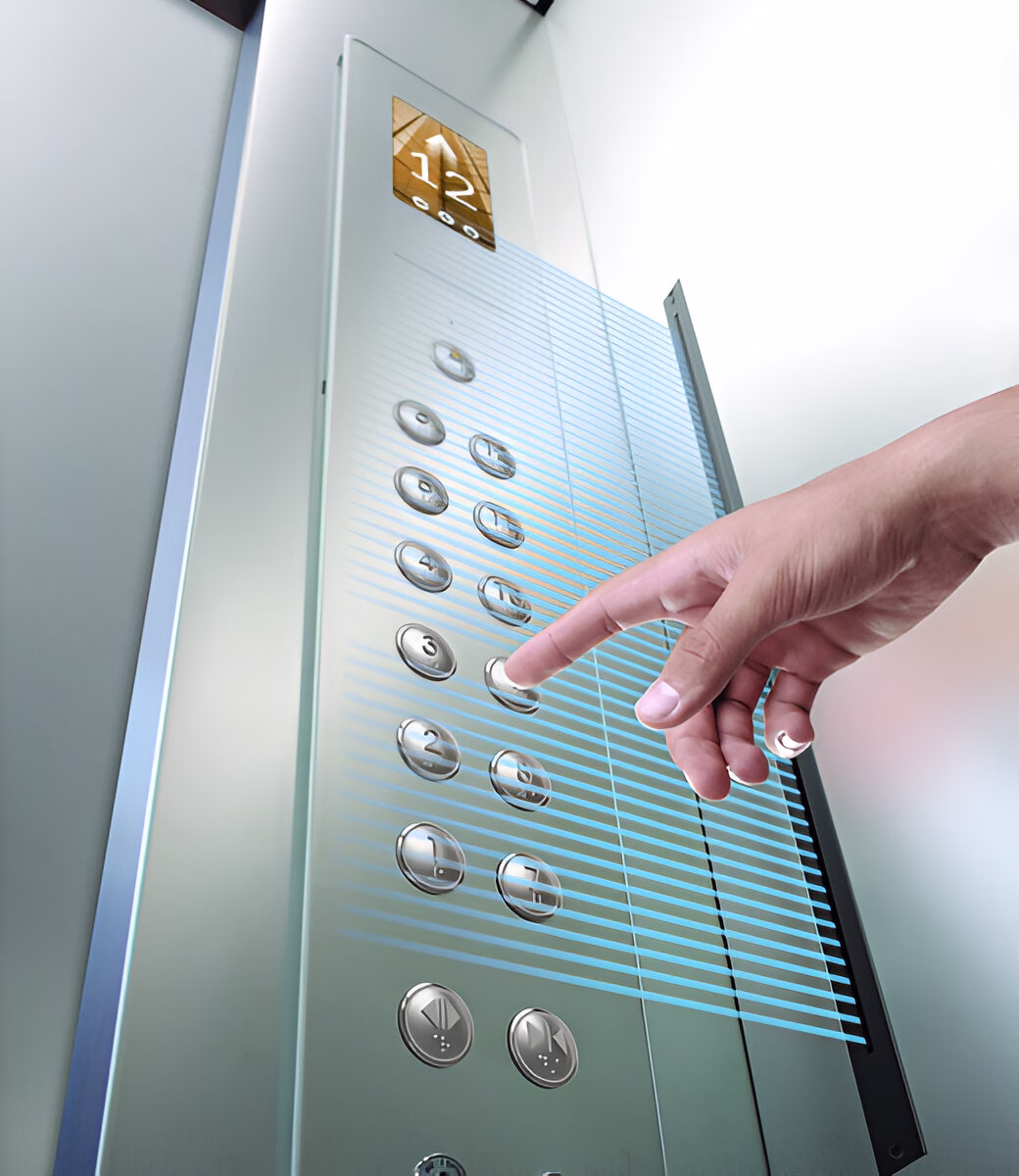 Рука натискає на кнопку '3' на сріблястій панелі керування ліфтом з підсвіченими кнопками поверхів та цифровим дисплеєм зверху, що показує '12' та стрілку вгору.