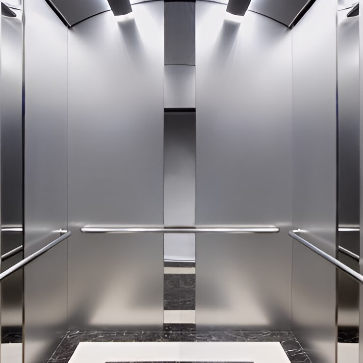 Інтер'єр сучасного ліфта з мінімалістичним дизайном. Кабіна має повністю металеві сріблясті стіни з поручнями по боках. У верхній частині розташовані вбудовані світильники, які створюють рівномірне освітлення. Підлога частково виконана з темного мармуру. Загальний дизайн підкреслює елегантну простоту та функціональність простору з використанням якісних матеріалів.