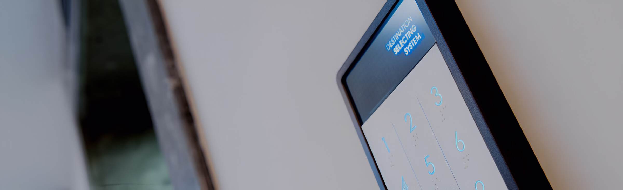 Зблизька знімок сенсорного екрана системи вибору поверху ліфта, розташованого на стіні, з відображеною цифровою клавіатурою та текстом 'DESTINATION SELECTING SYSTEM' (система вибору пункту призначення) у верхній частині.