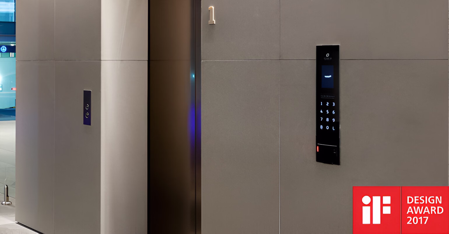 Фрагмент інтер'єру з дверима ліфта з вертикальною панеллю виклику праворуч, що має цифровий дисплей та сенсорні кнопки з підсвічуванням. У нижньому правому куті розміщено логотип 'iF DESIGN AWARD 2017'. Ліворуч видно ще одні двері ліфта з вертикальною панеллю з двома кнопками зі стрілками.
