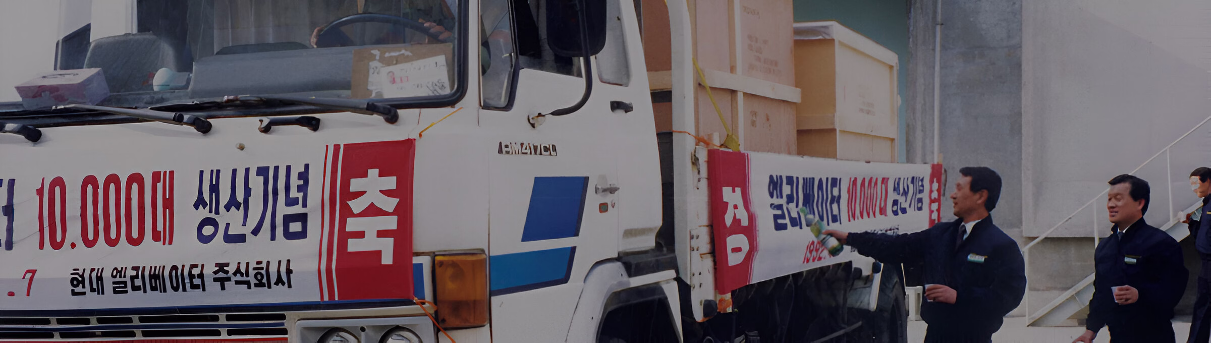 Біла вантажівка Hyundai Elevator з написом '110 000 виробничих одиниць' корейською мовою, оточена людьми, які, ймовірно, святкують цю подію.