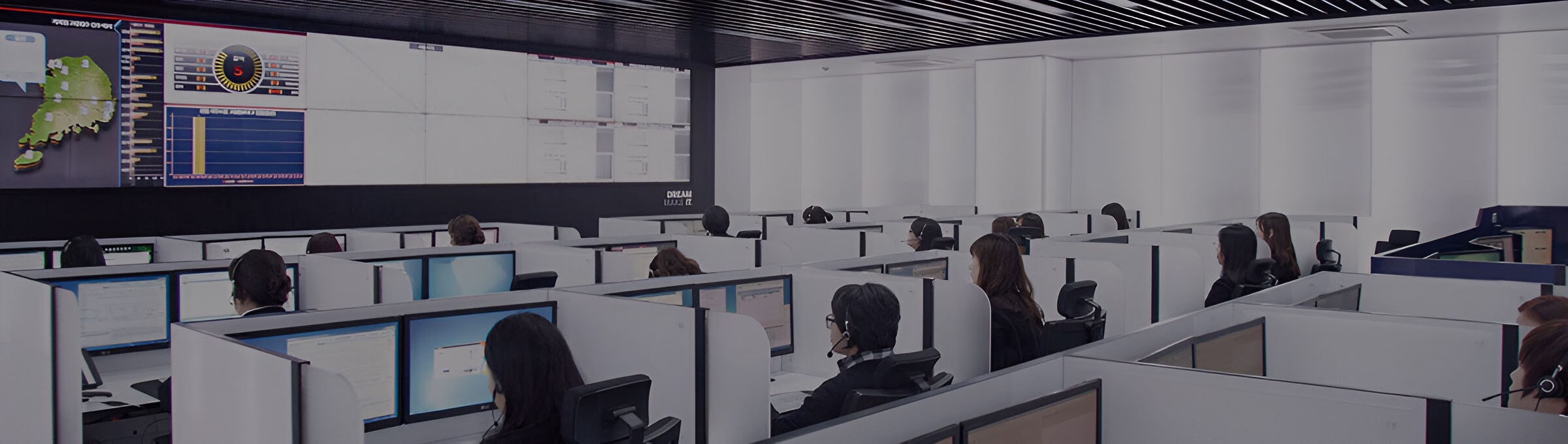 Внутрішній вигляд центру моніторингу або керування з рядами робочих місць, де оператори сидять перед комп'ютерами, а на задньому плані велика відеостіна відображає дані, карти та графіки.