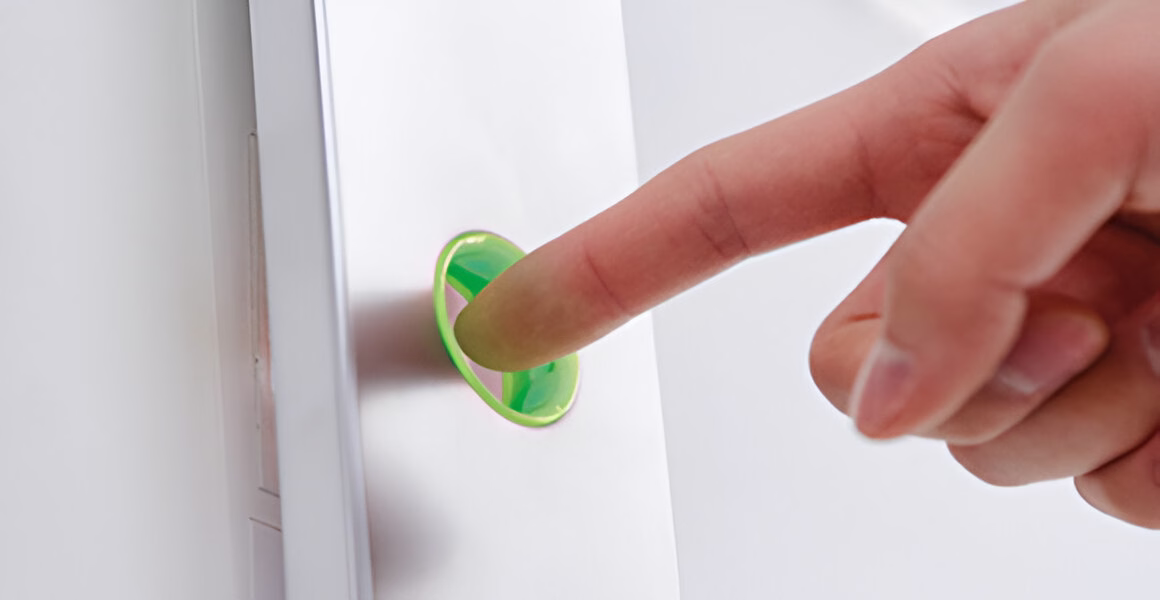 Крупний план пальця, що натискає на круглу зелену кнопку, вбудовану в білу поверхню.