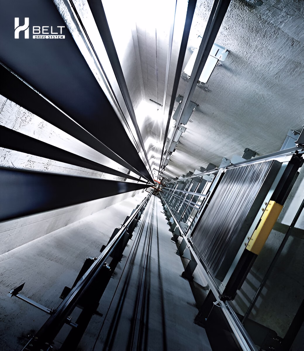 Вигляд зсередини ліфтової шахти, що прямує вгору, з рейками, противагою та тросами, освітленими зверху.