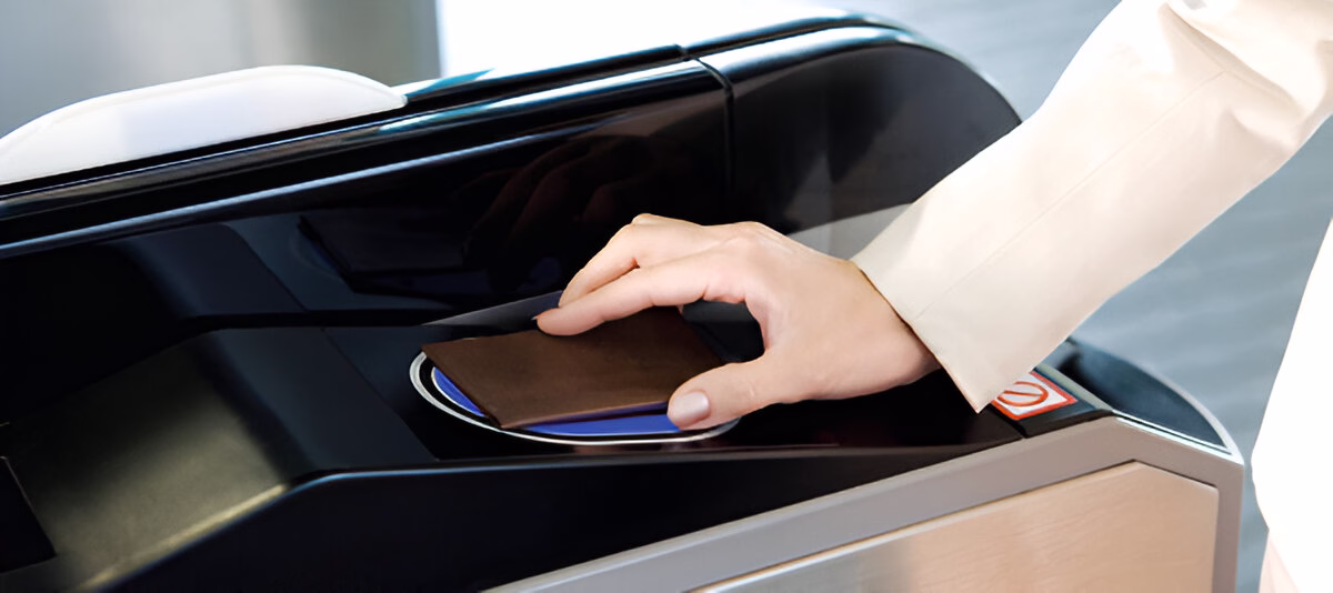 Рука людини прикладає паспорт до зчитувача на електронному турнікеті для ідентифікації або проходу через контрольний пункт.