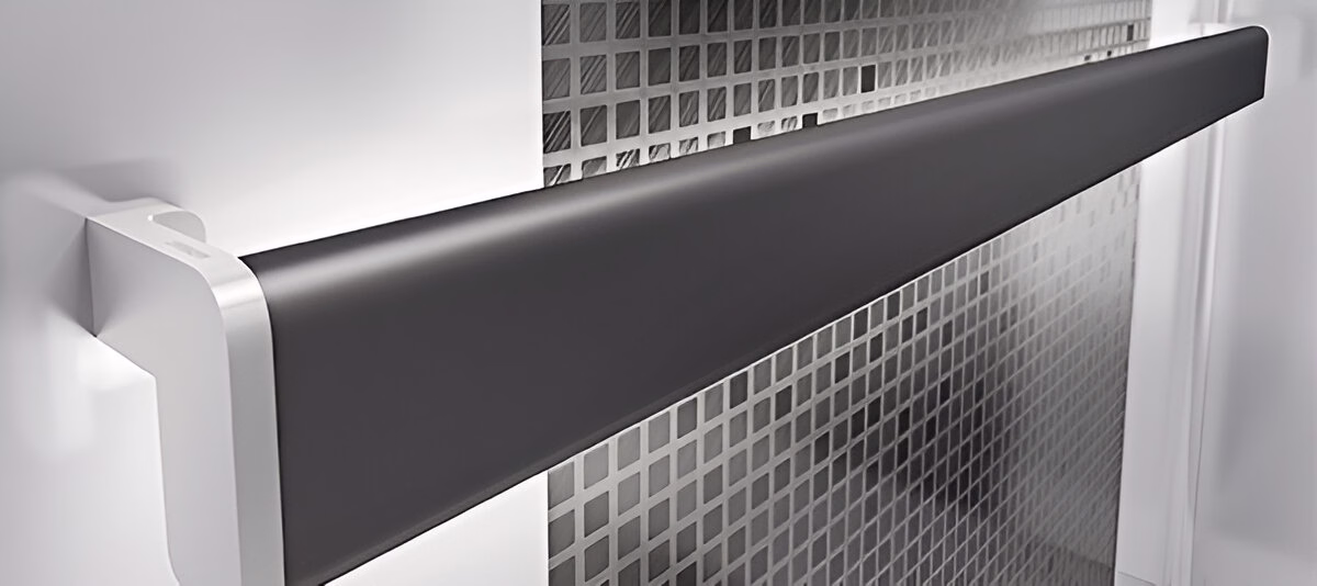 Чорний поручень овальної форми, прикріплений до білого кронштейна на світлій стіні з квадратним текстурованим візерунком.